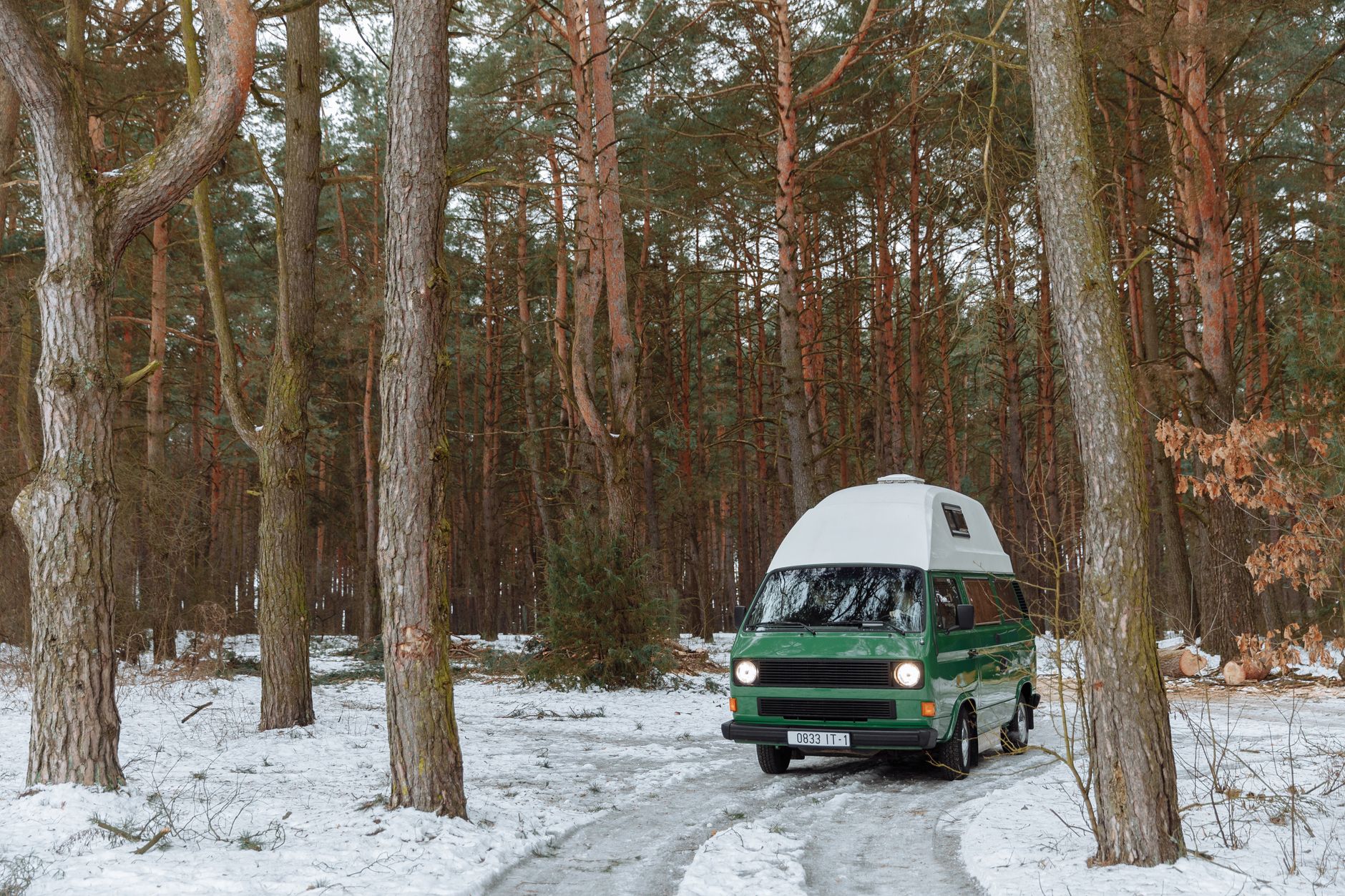 Vintage campervan parked in a snowy forest, encapsulating a serene winter camping vibe.