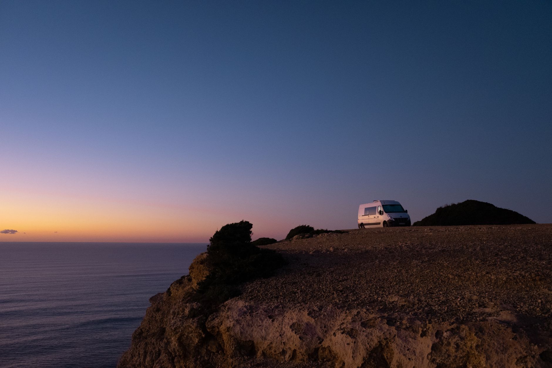 A tranquil van parked on a cliff overlooking the ocean at sunset, showcasing serene travel vibes.